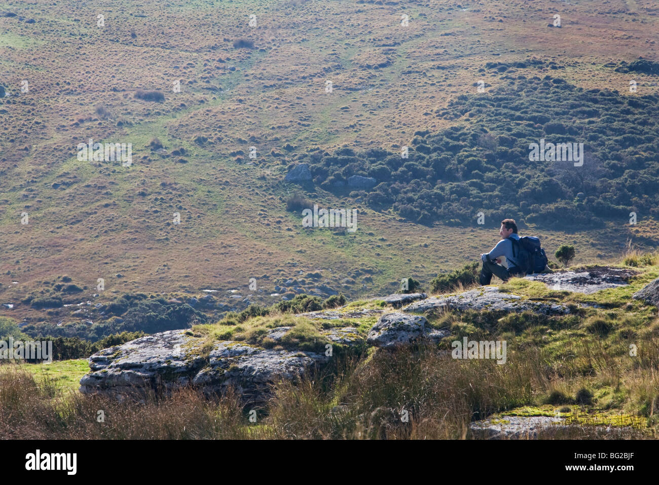Uomo seduto su Dartmoor tor guardando in spazio aperto Foto Stock