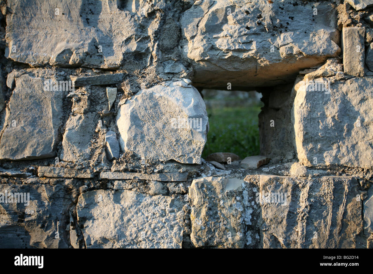 Finestra piccola apertura attraverso il vecchio muro di pietra, erba visibile Foto Stock