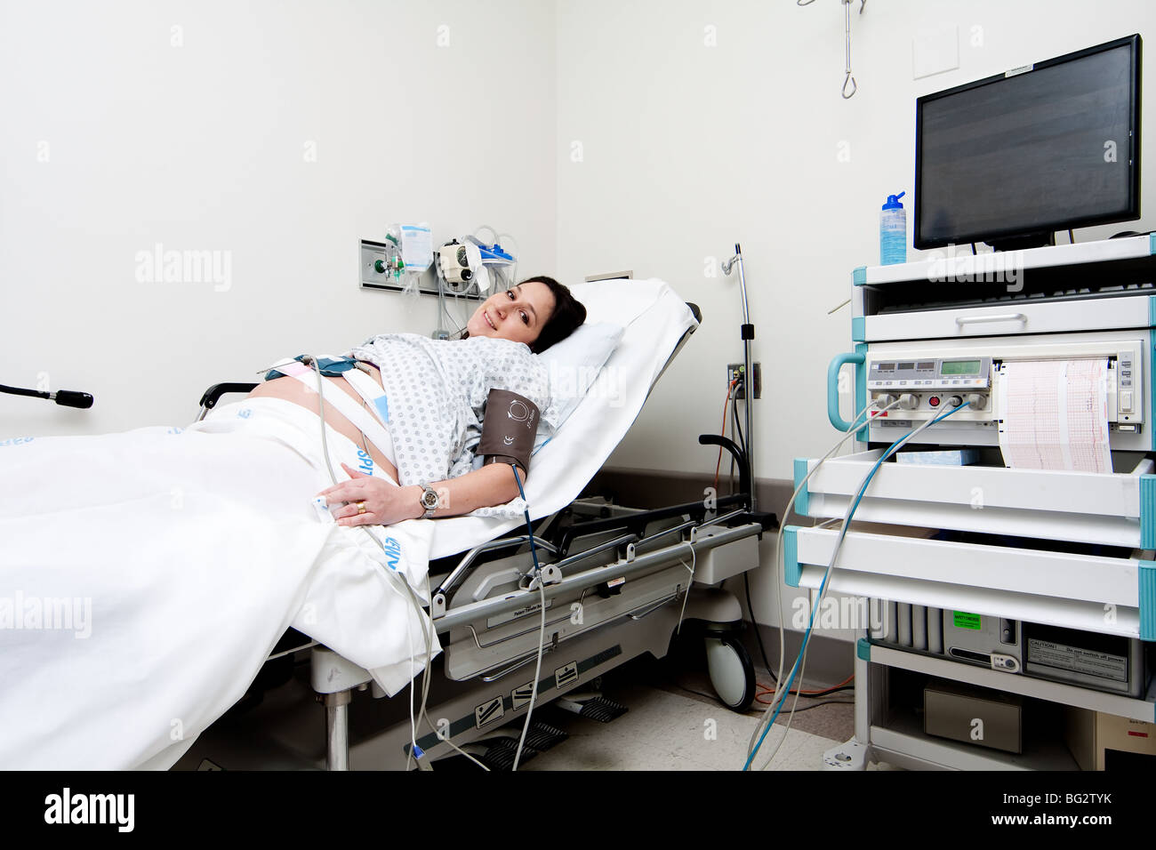 Gravidanza ispanica caucasica Latina donna posa in un ospedale gurney letto nell'unità triage facendo un medico di non-stress test. Foto Stock