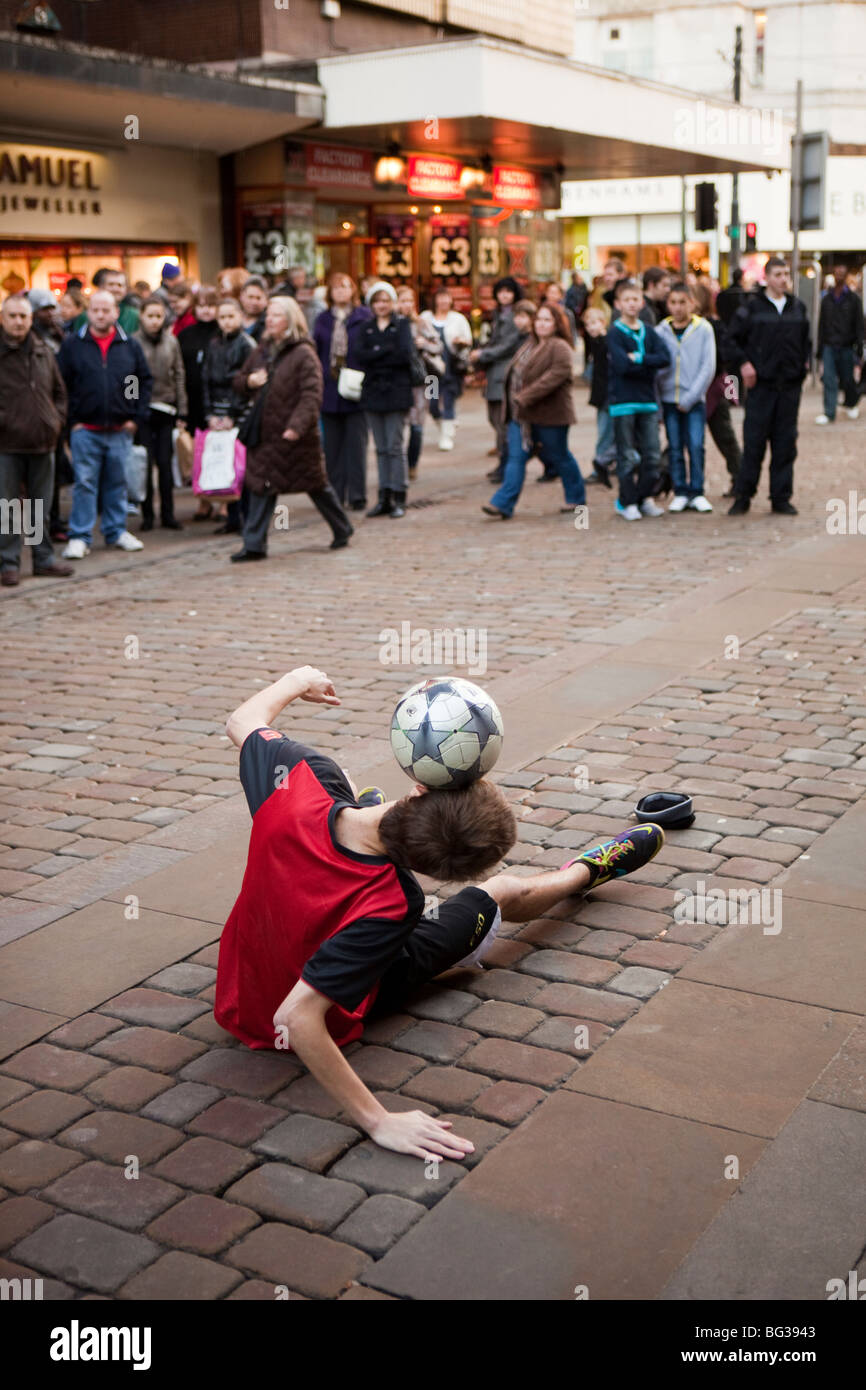 Regno Unito, Inghilterra, Manchester, Market Street, calcio suonatore ambulante di giocoleria sfera di bilanciamento sulla testa Foto Stock