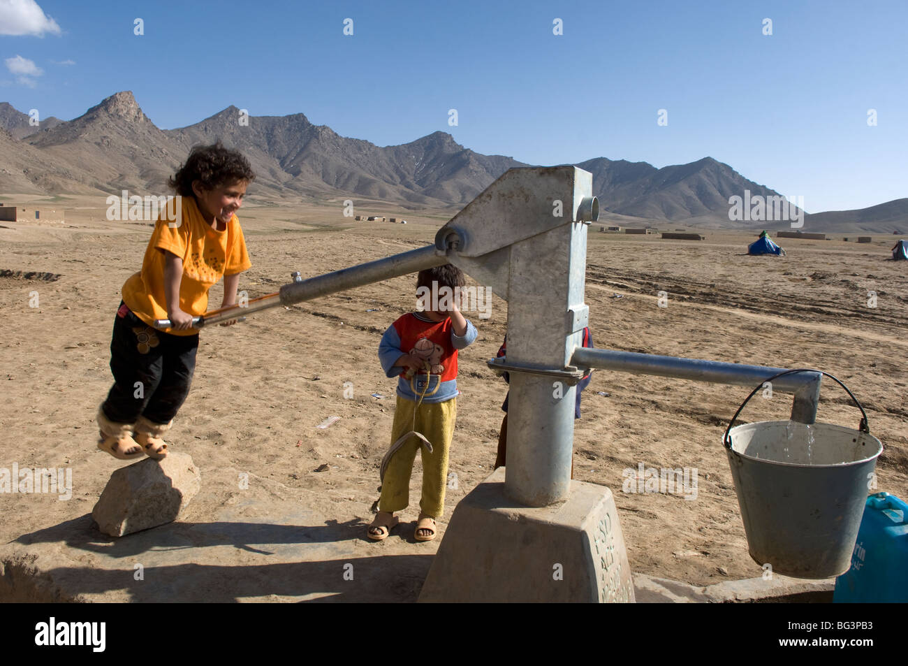 Bambini afgani di pompare acqua dal bene il terreno in Bagram, Afghanistan. Foto Stock