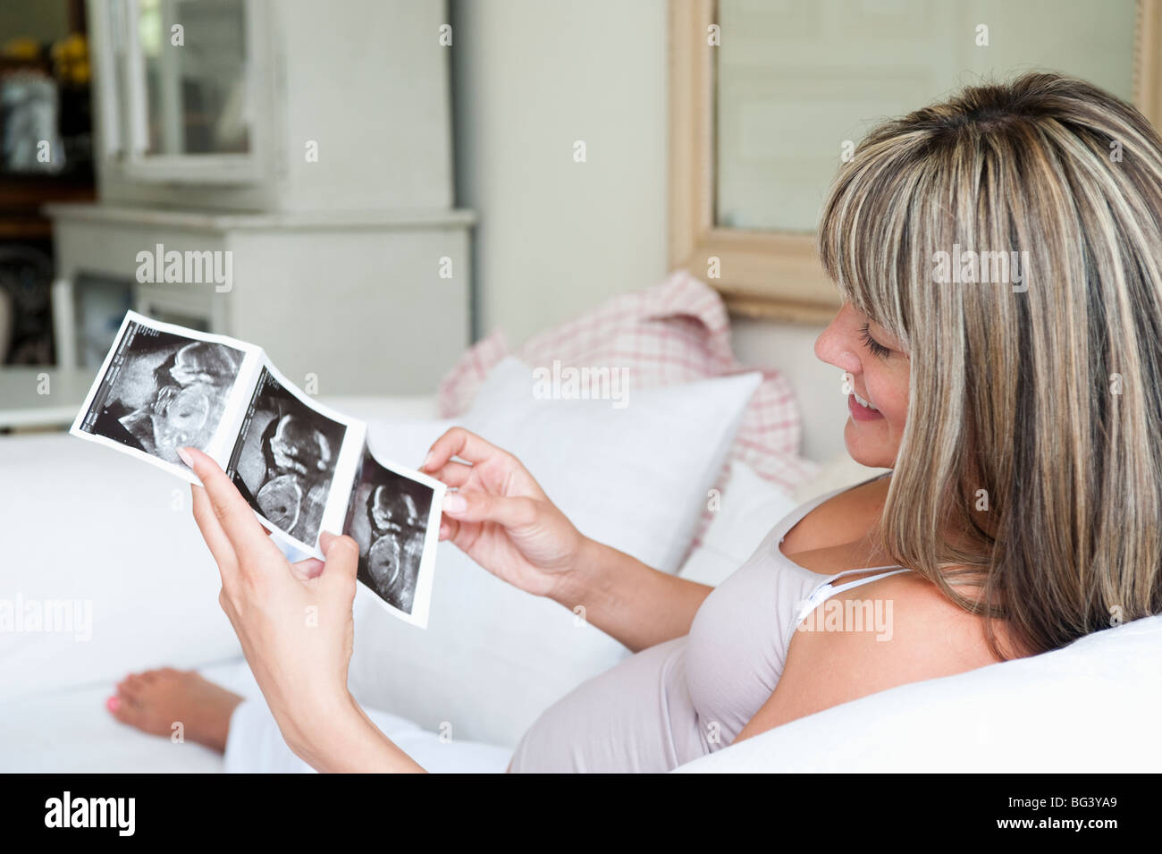 Donna incinta seduta sul divano con baby scan Foto Stock