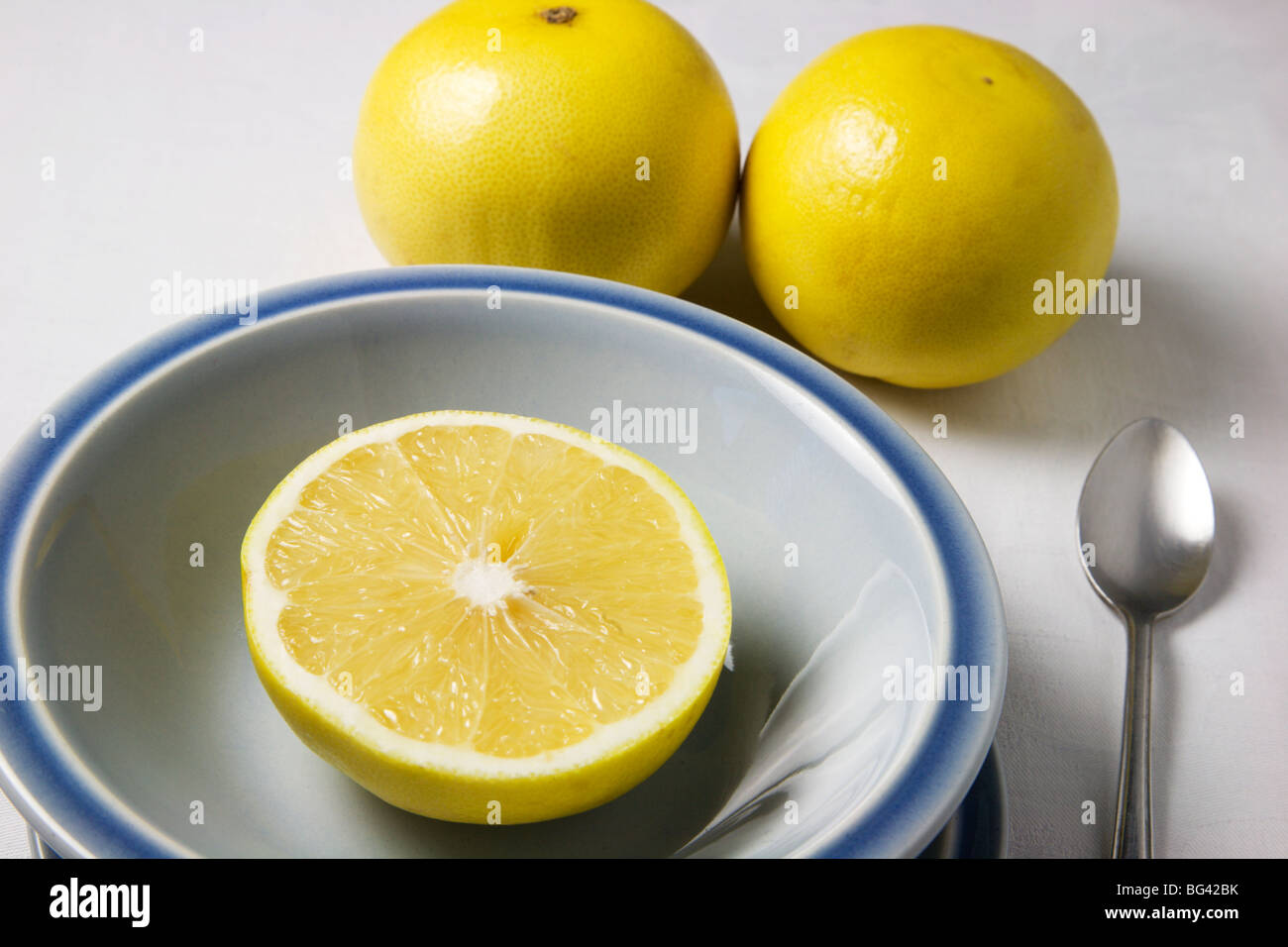 Mezzo pompelmo in una ciotola blu e pompelmo intero su una tovaglia bianca Foto Stock