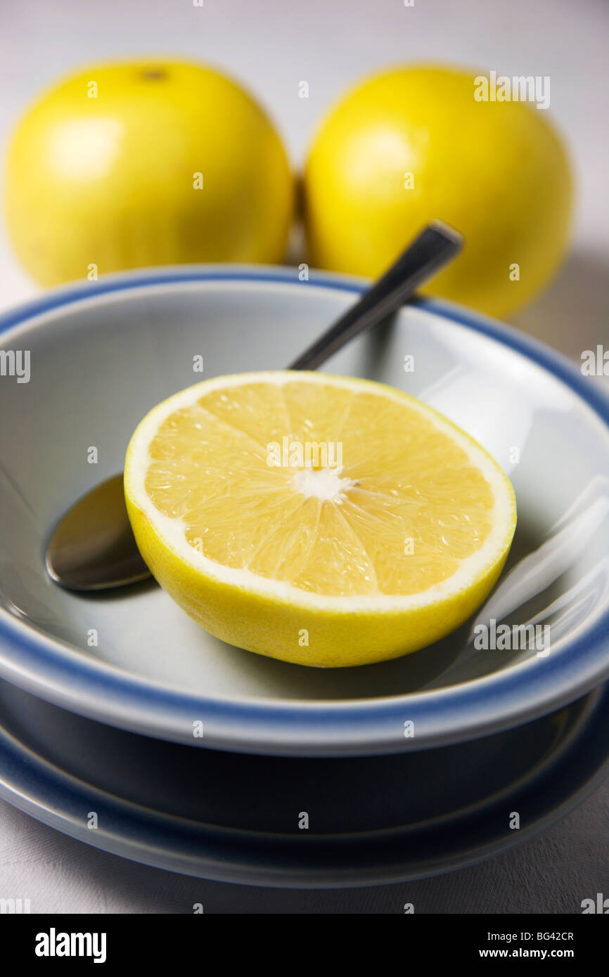 Mezzo pompelmo in una ciotola blu e pompelmo intero su una tovaglia bianca Foto Stock