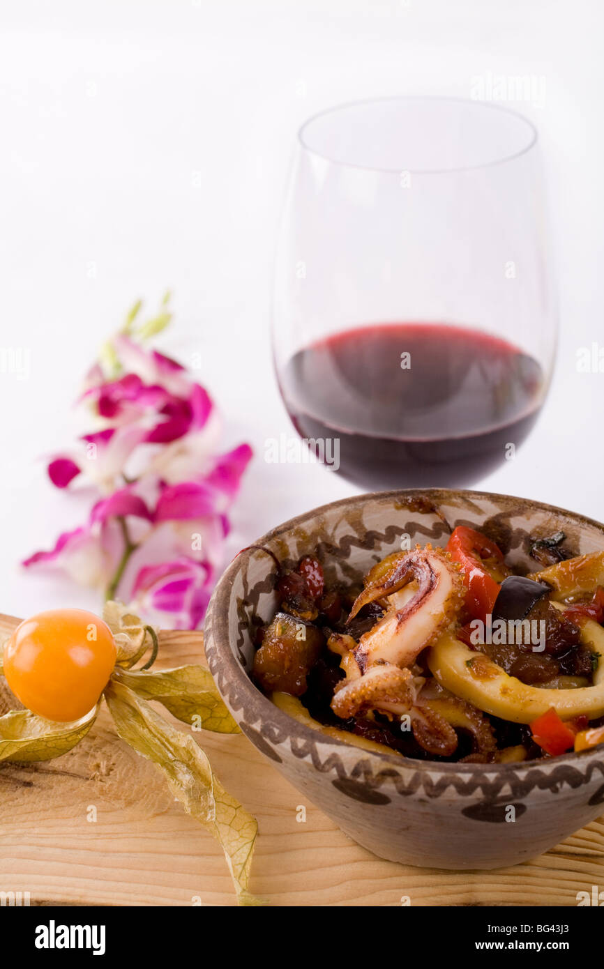 Un antipasto di calamari, polpi e verdure speziato, con un bicchiere di vino rosso. Foto Stock