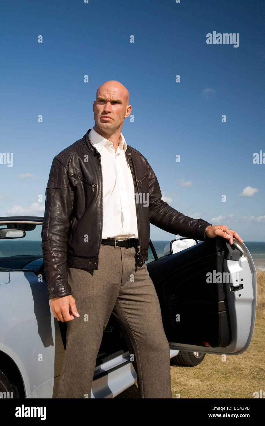 Uomo in piedi con la sua Aston Martin Vantage sulla scogliera Foto Stock