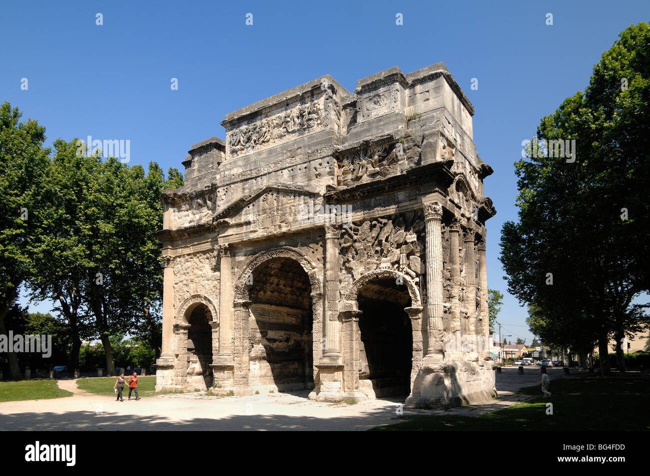 Coppia a piedi dall'Arco Romano di Trionfo o Arco Trionfale di Orange (c20BC), architettura classica Romana, Orange, Vaucluse, Provenza, Francia Foto Stock