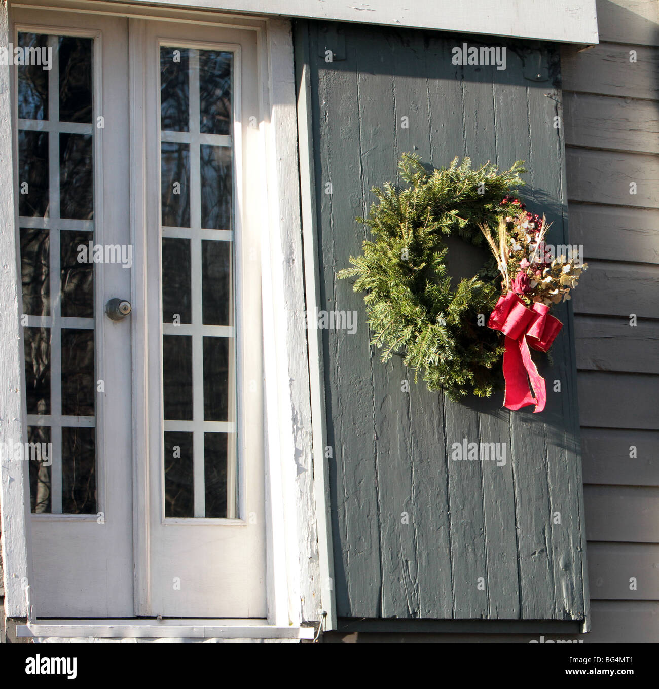 Una ghirlanda di Natale con un fiocco rosso su una serranda di una vecchia casa storica. Tempi coloniali vintage shot. Foto Stock