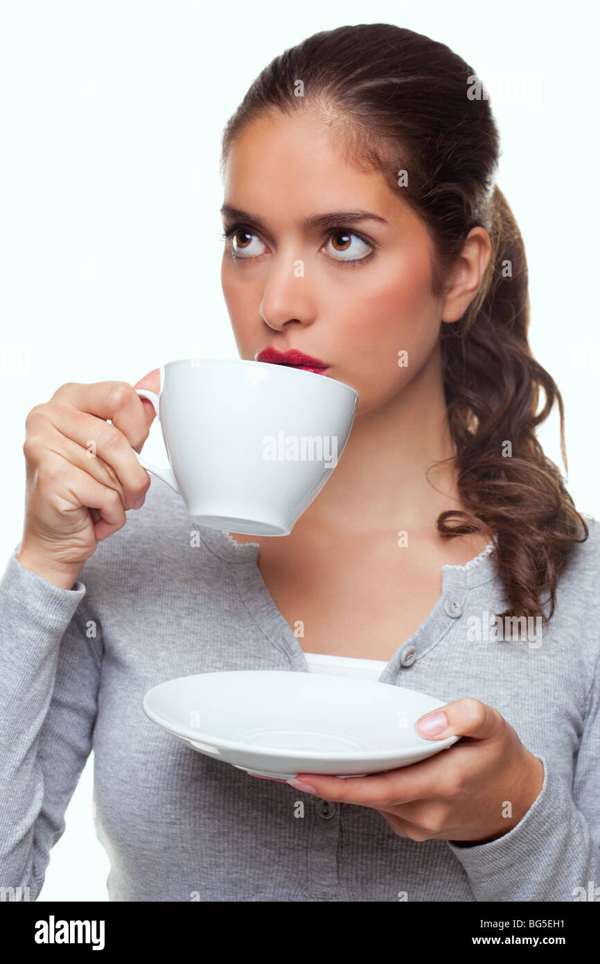 Una donna bere il tè da una tazza e piattino come lei sta pensando a qualcosa, sfondo bianco. Foto Stock
