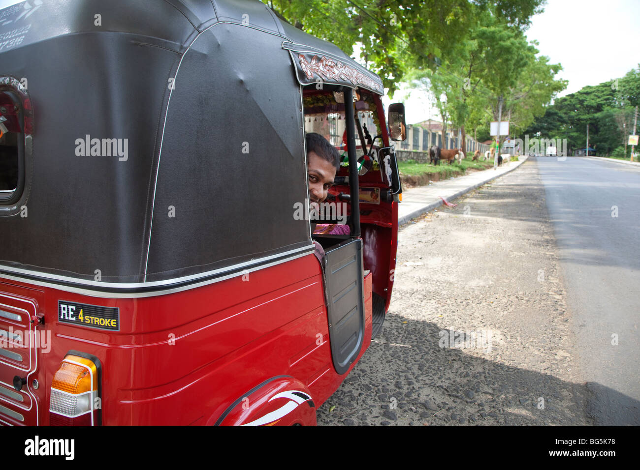 Un tuk tuk conducente prende un periodo di riposo dal lato strada. Sri Lanka Foto Stock