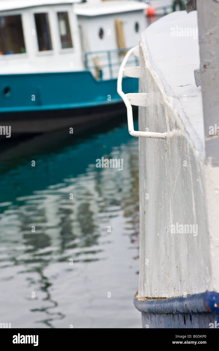 L'angolo di una vecchia barca, che mostra la struttura di scafo verniciato con un altra barca e riflessi nell'acqua dietro. Foto Stock