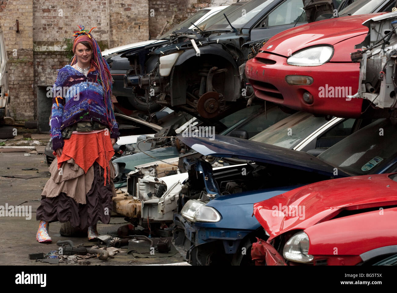 Modello femminile in auto nel cortile di scarto con luminosi abiti colorati e i capelli. Modello completamente rilasciato Foto Stock