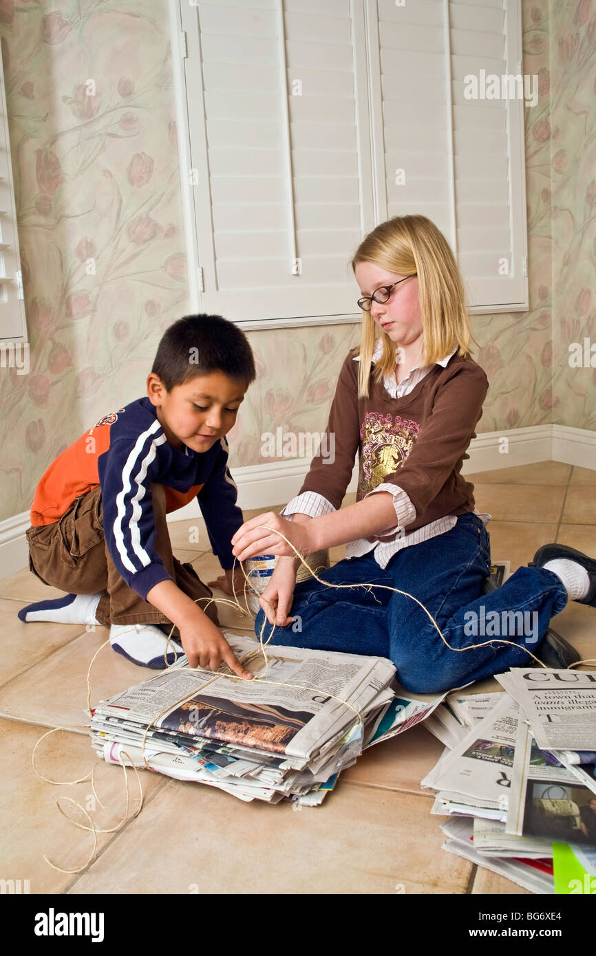 Ispanico 5-6 ragazzo e ragazza caucasica 8-10 anni di lavorare insieme al pacchetto quotidiani per il riciclo di aiutare i bambini bambino aiutando un altro servizio signor © Myrleen Pearson Foto Stock