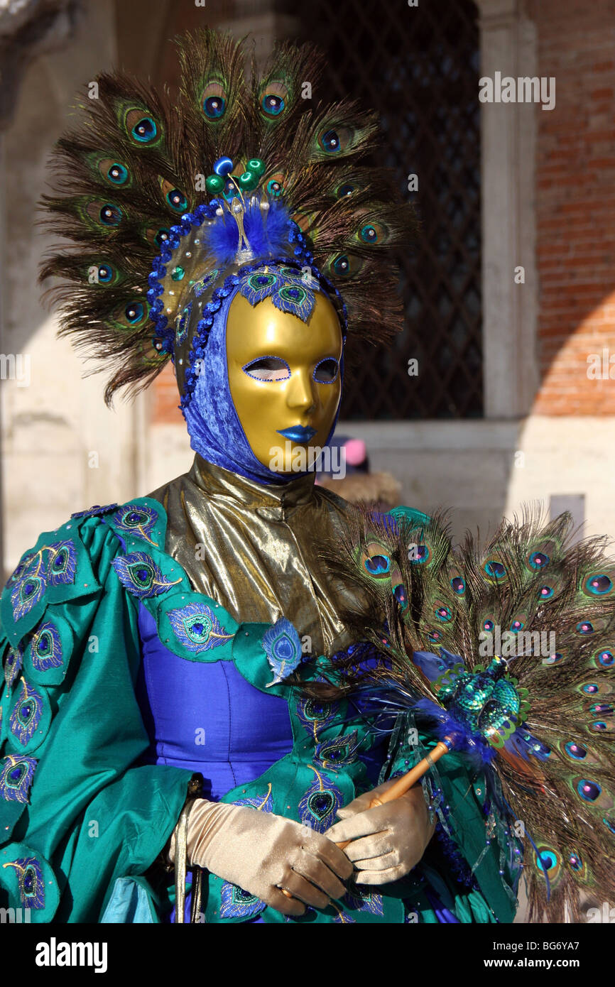 Close-up di un veneziano di donna che indossa una maschera d'oro e una blu  e verde decorata in costume con penne di pavone, il Carnevale di Venezia  Foto stock - Alamy