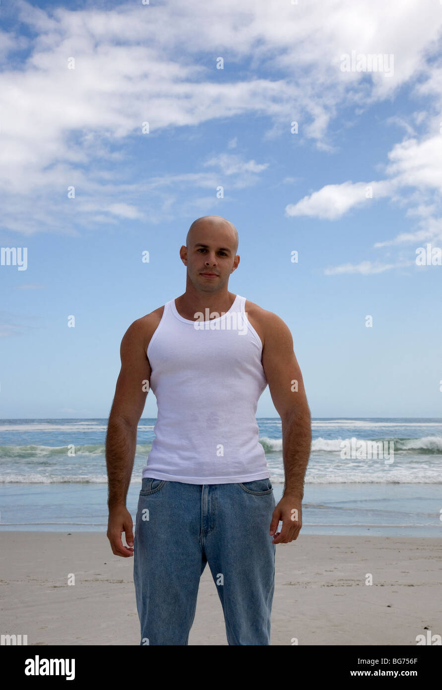 Muscoloso uomo Giubbotto in jeans e sulla spiaggia - bracci ripiegati Foto Stock