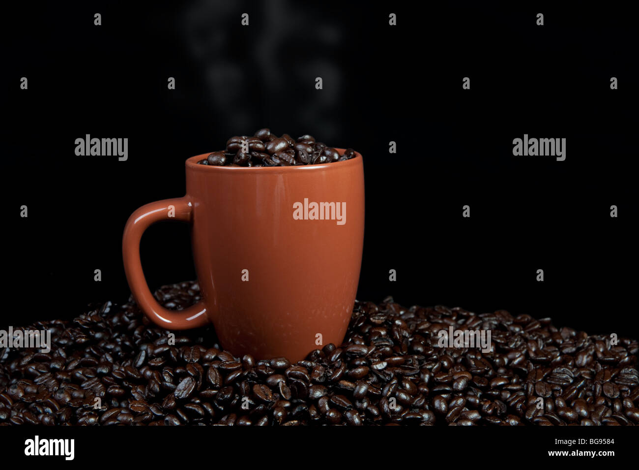 Tazza di chicchi di caffè seduti sulla cima di chicchi di caffè con vapore che salgono dal bicchiere. Foto Stock