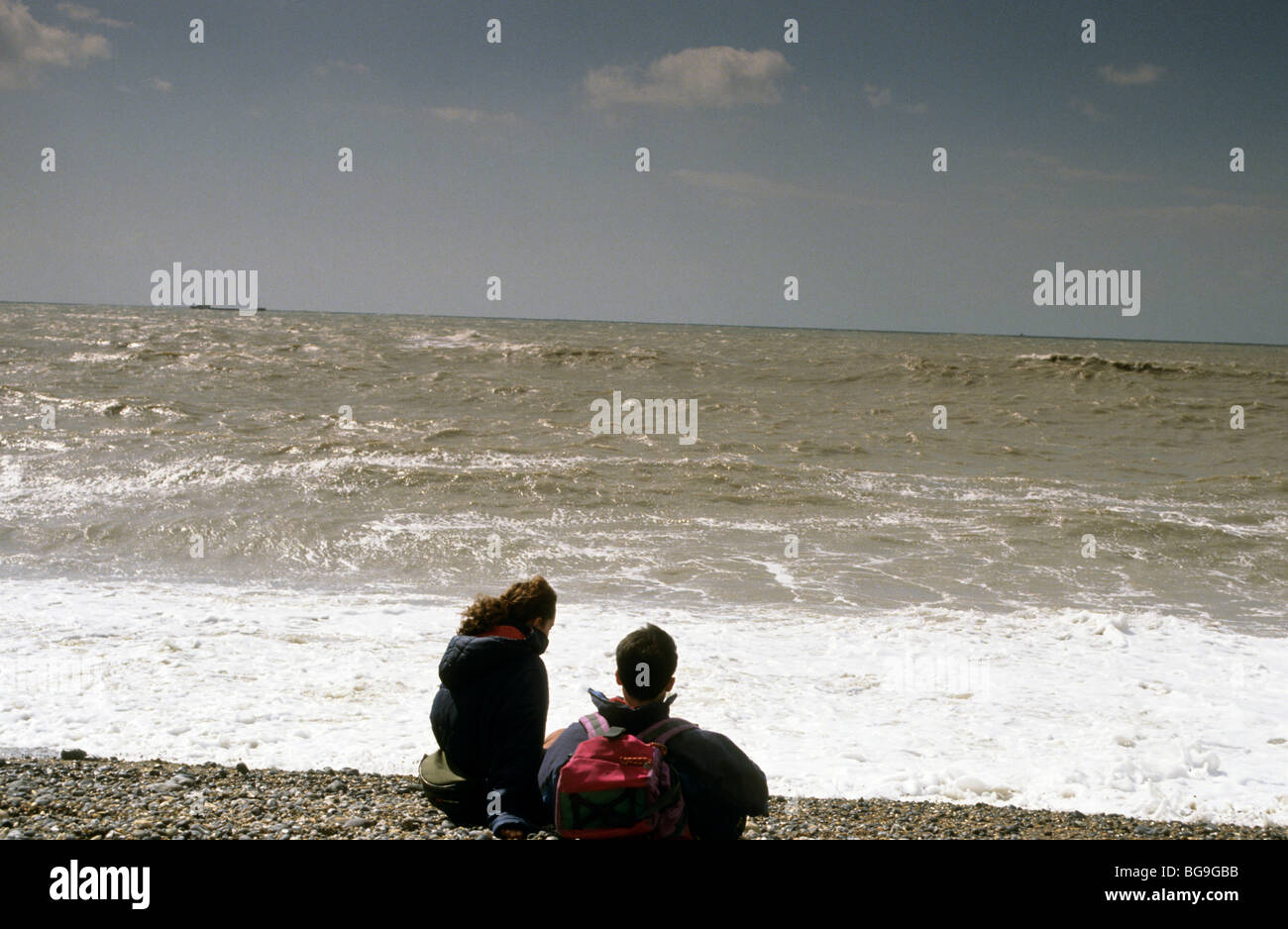Due escursionisti seduto sulla spiaggia guardando le onde che si infrangono Foto Stock