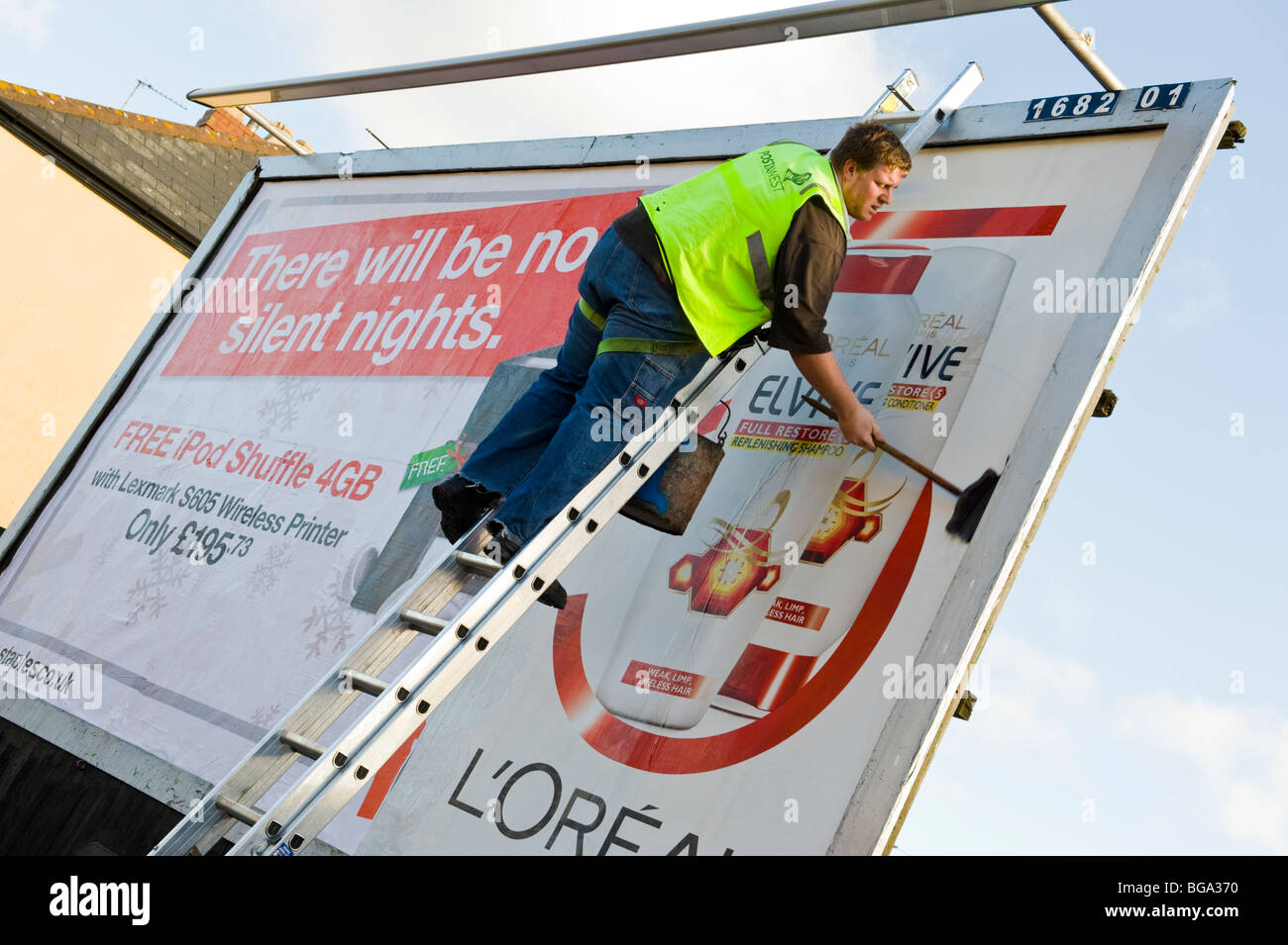 Lavoratore di scala con manico lungo pennello incollare poster pubblicitario sul sito di Billboard in Newport South Wales UK Foto Stock