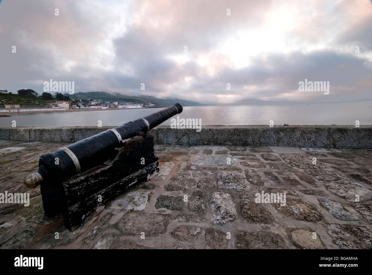 Il cannone sulla parete del porto allo spuntar del giorno a Lyme Regis Foto Stock