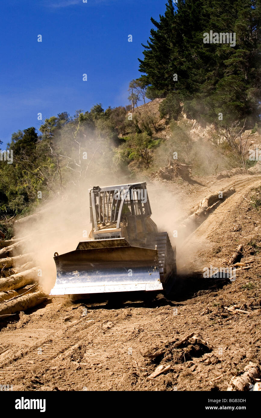 Bulldozer la guida verso il basso polverosa strada forestale con alberi di pino e registri Foto Stock