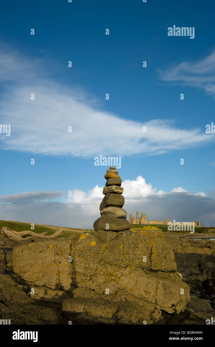 Una rilassante pila di rocce con il castello di Dunstanburgh visibile in distanza Foto Stock