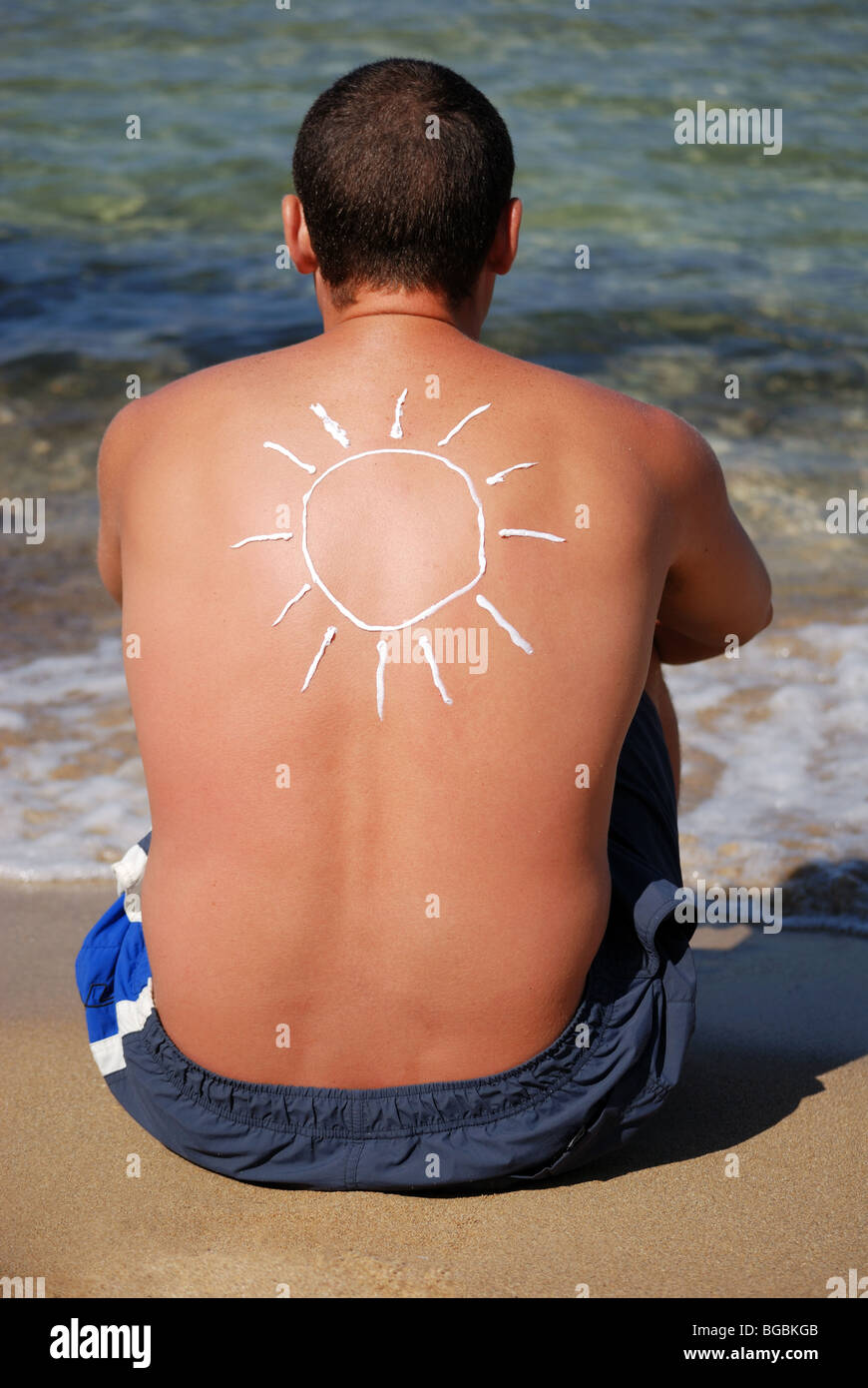 Giovane uomo seduto sulla spiaggia con sole foto fatta da una lozione Foto Stock