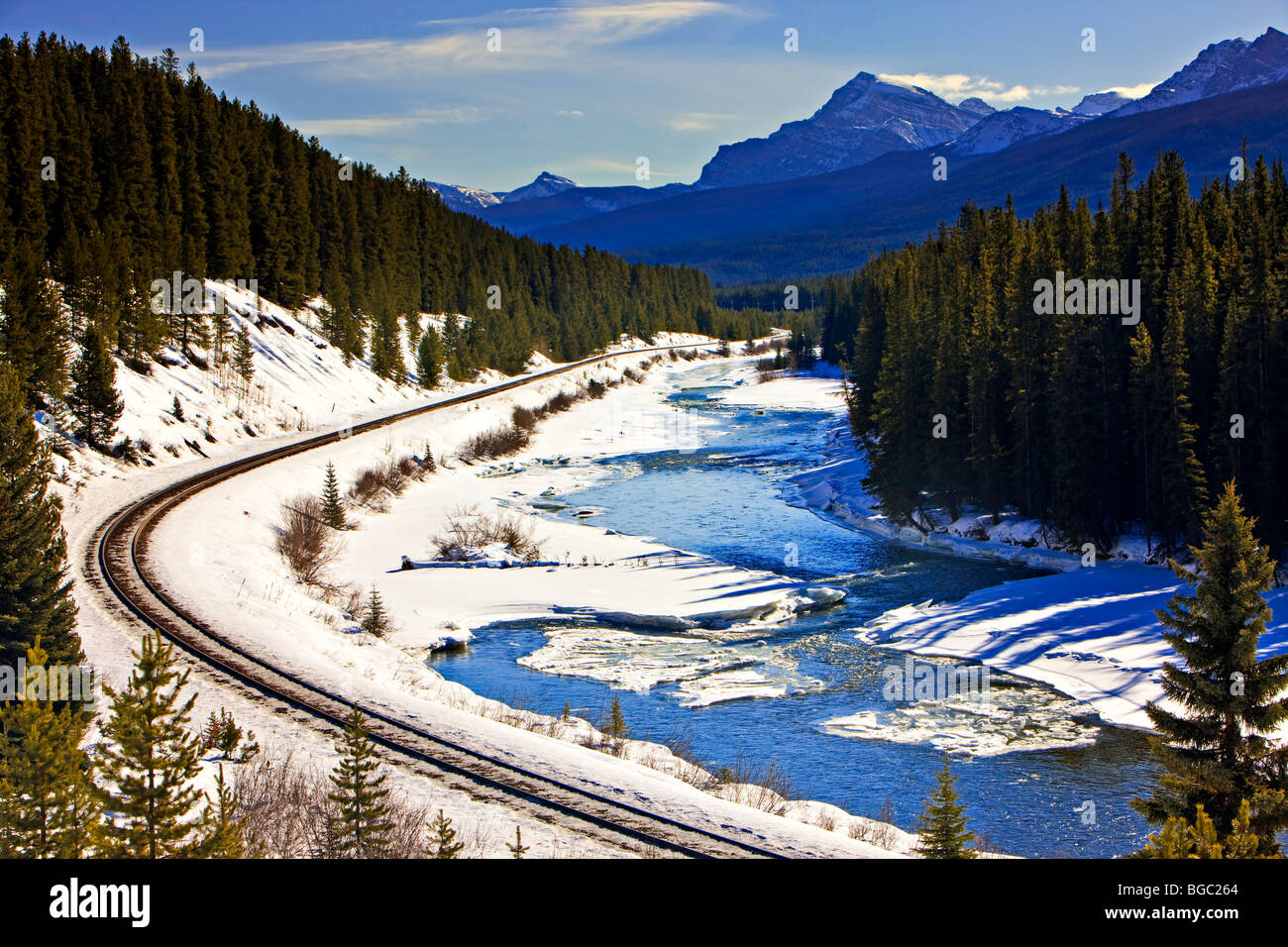 Avvolgimento di binari ferroviari accanto alla neve e ghiaccio orlata Fiume Bow durante l'inverno, il Parco Nazionale di Banff, Canadian Rocky Mountains, un Foto Stock