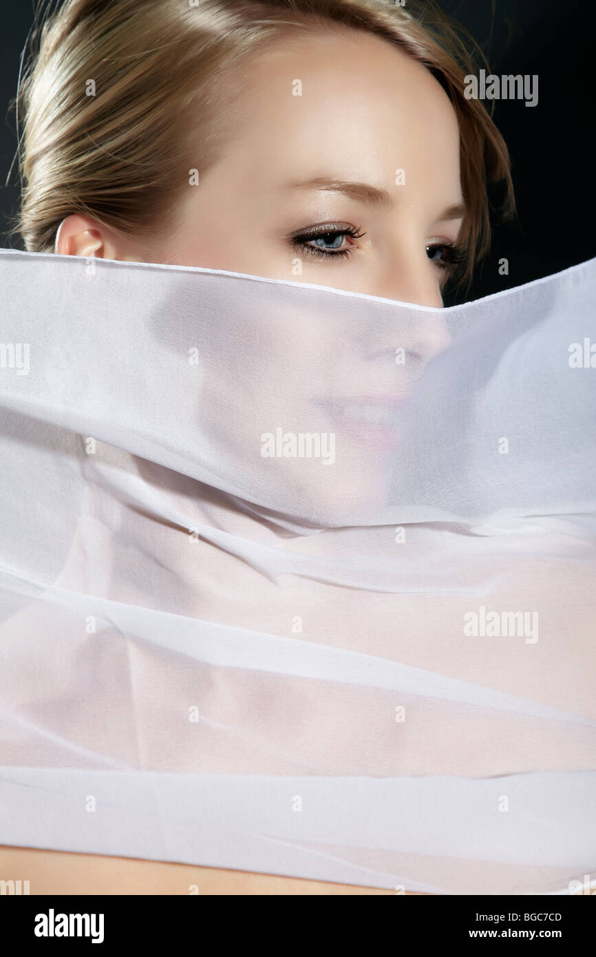 Ritratto di una giovane donna con un fluire di seta bianca tessuto nella parte anteriore del suo viso Foto Stock