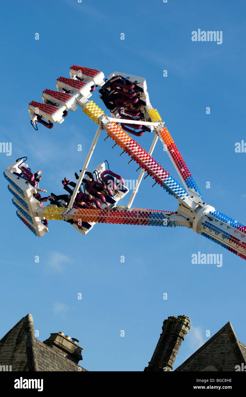 Freak Out fairground ride alla sommità del pendolo incorniciata su un angolo con Tetti e camini di seguito, Tavistock Fiera d'oca, Devon Foto Stock