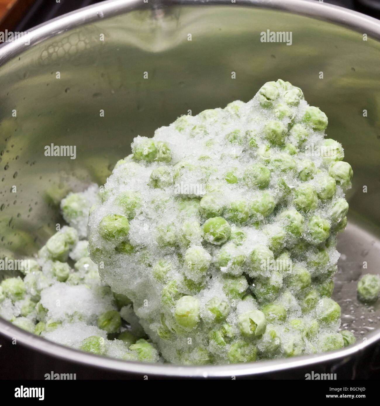 Pila di congelati petit pois piselli in acciaio stanless pentola in attesa di essere riscaldato su stufa. Foto Stock