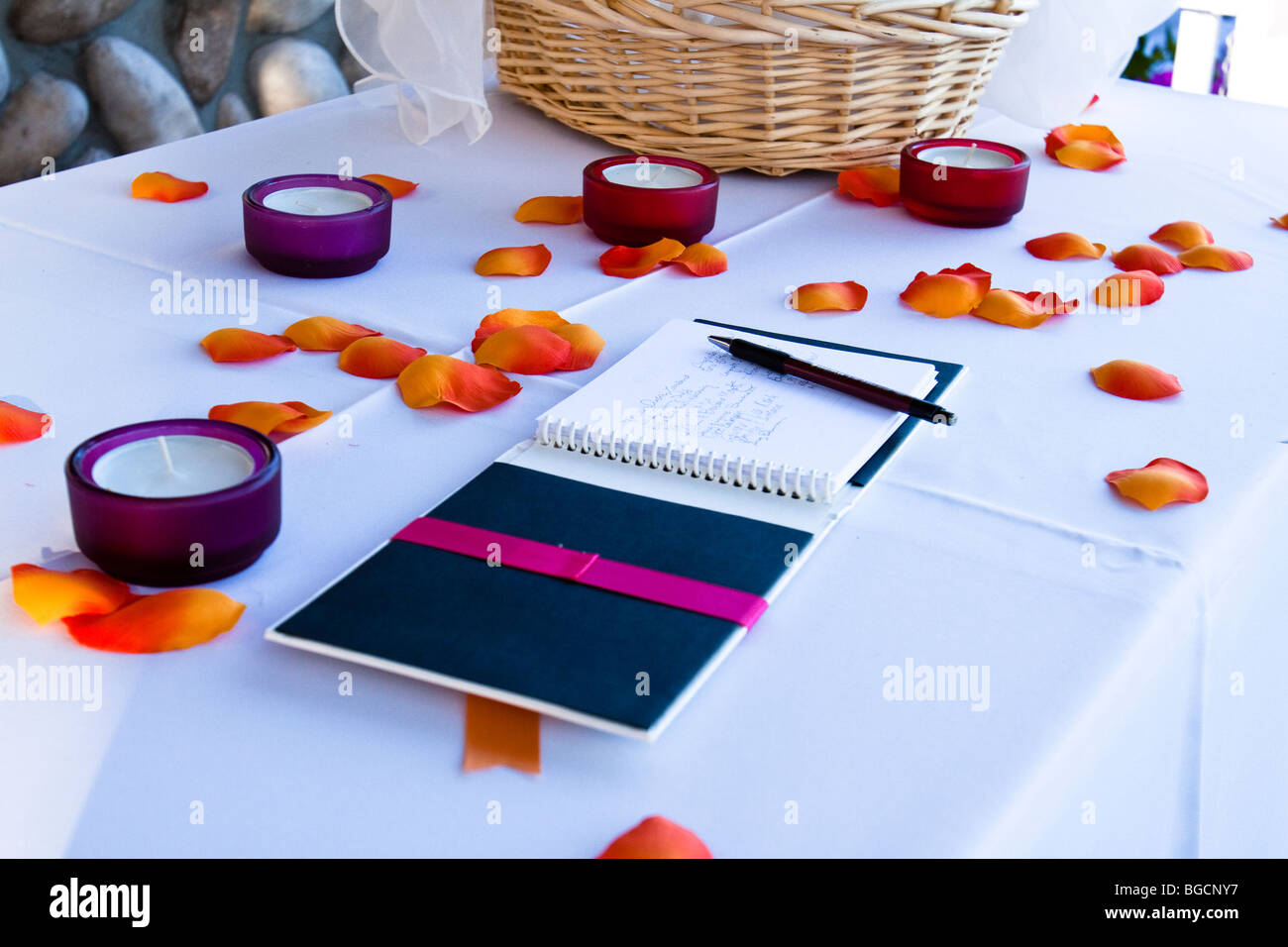 Wedding guest book con firme su una tabella con petali di fiori e candele votive Foto Stock