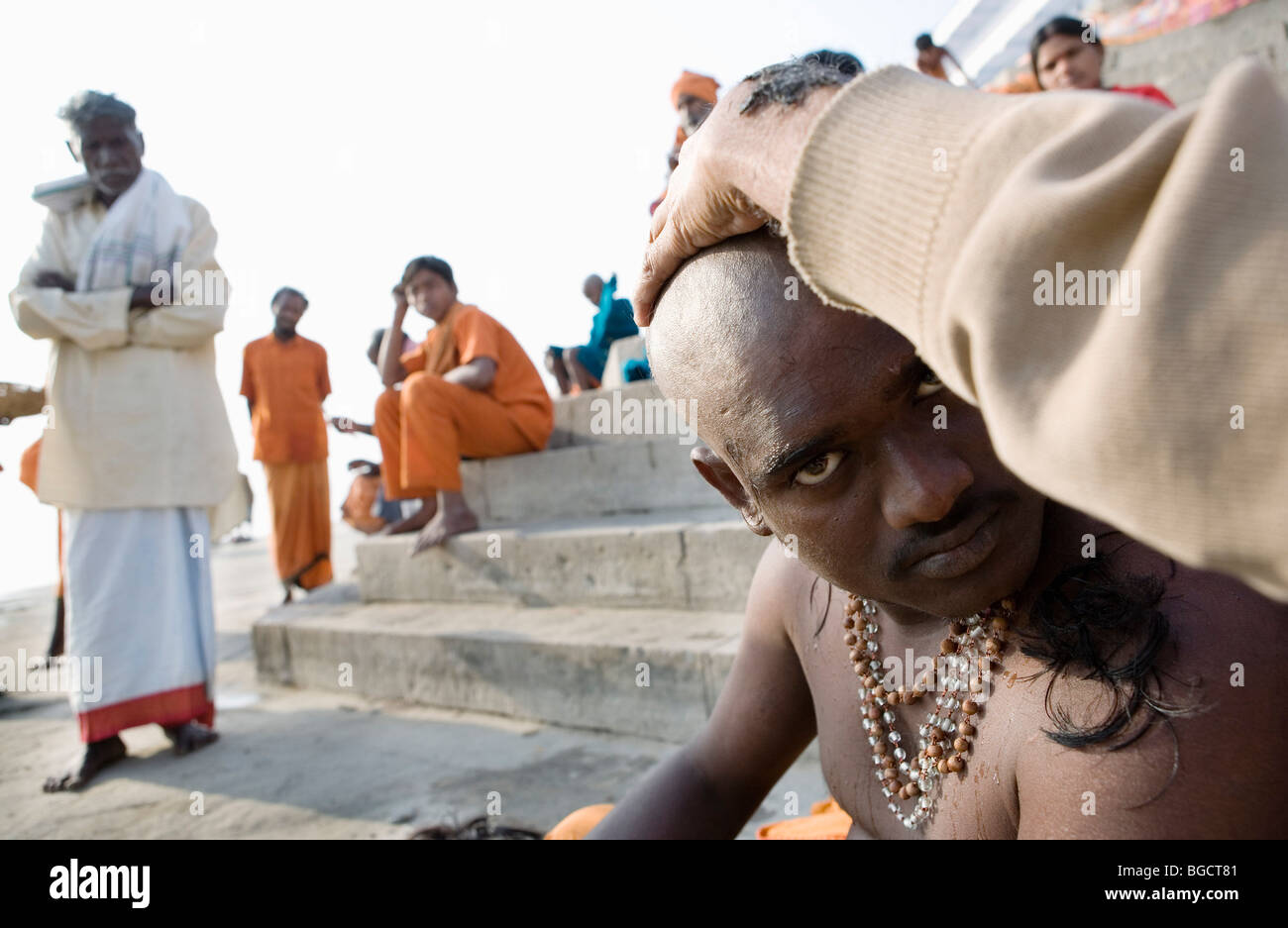 Pellegrini indù uomo avente la sua testa ritualmente radere al fiume Gange, Varanasi (India). Foto Stock