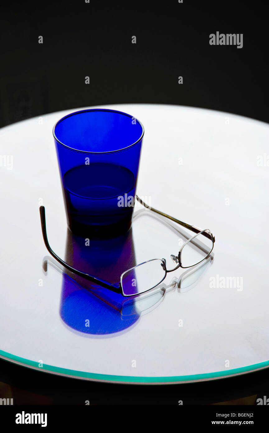 Vetro blu di acqua & Occhiali sul Round lucido tavolo riflettente Foto Stock