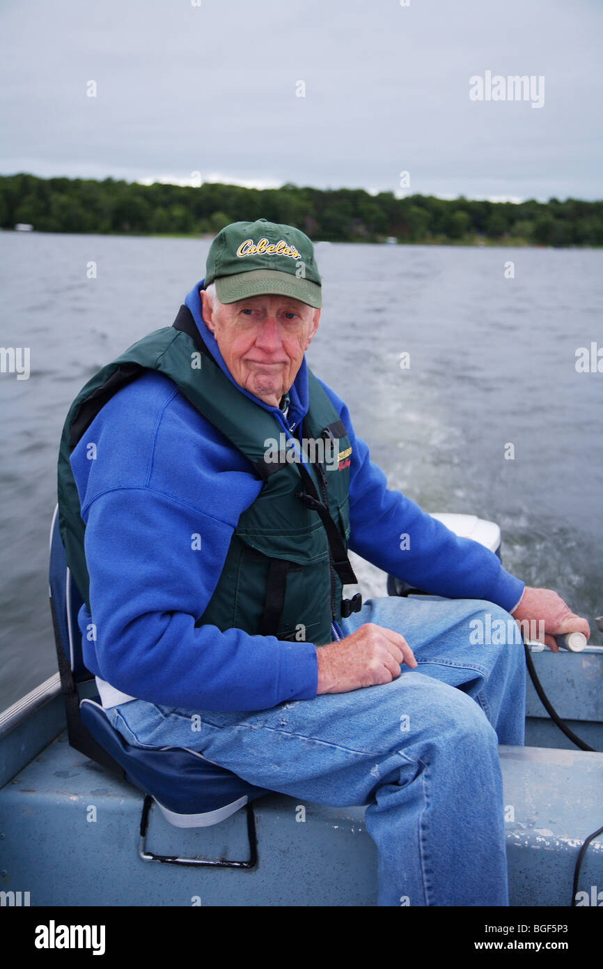 Senior anziani condito guida di pesca la guida alumnacraft barca da pesca nel freddo umido meteo instabile acqua onde wake azione Foto Stock