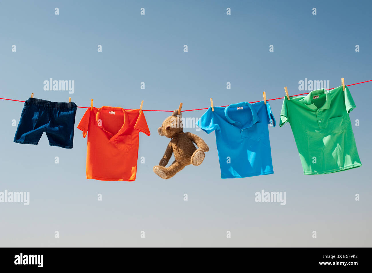 Abbigliamento per bambini e orso di peluche su una linea di lavaggio contro un cielo blu. India Foto Stock