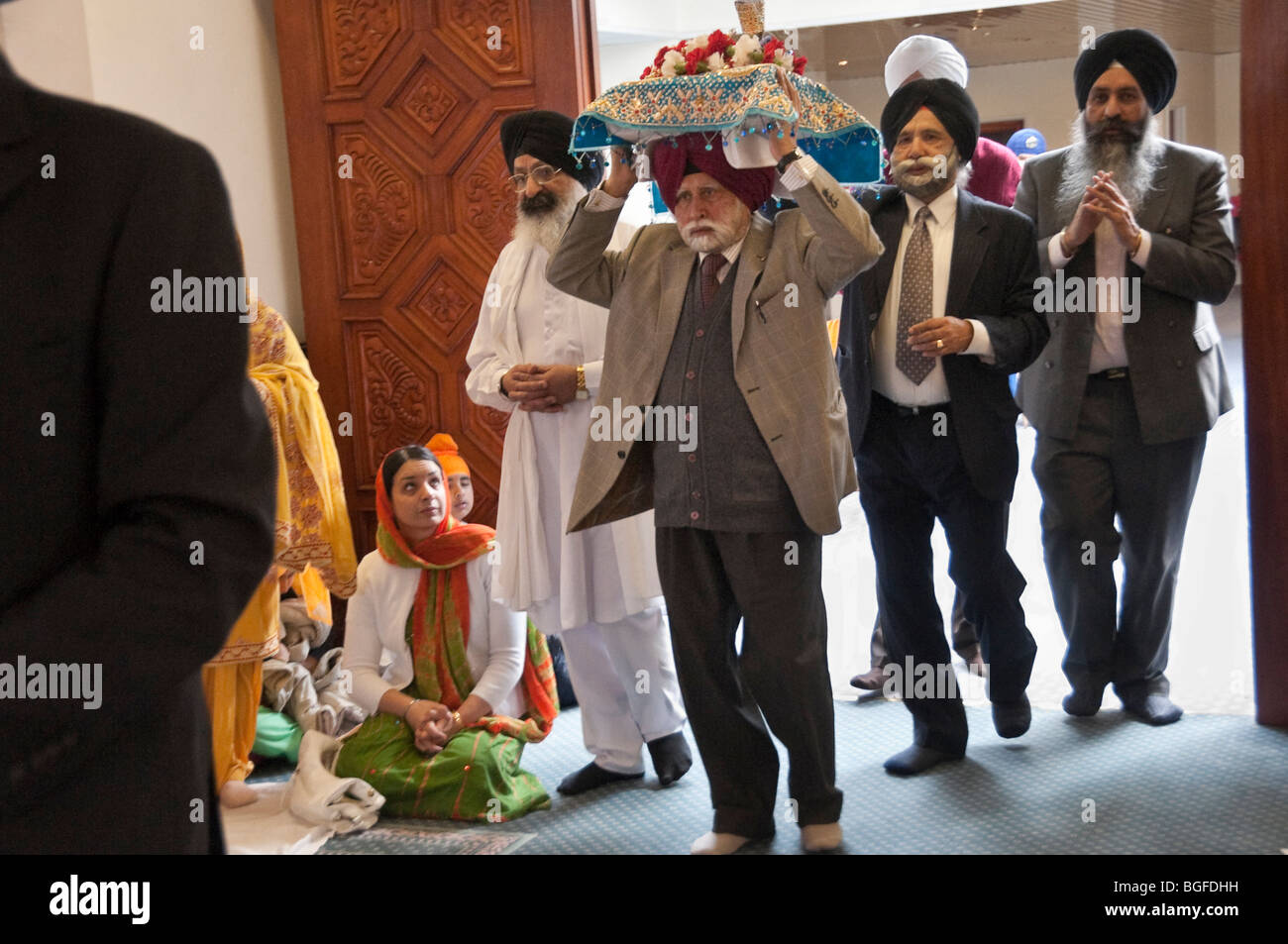 Il Guru Granth Sahib è portato nella sala culto a Hounslow Gurdwara su un anziano la testa prima della processione Vaisakhi Foto Stock