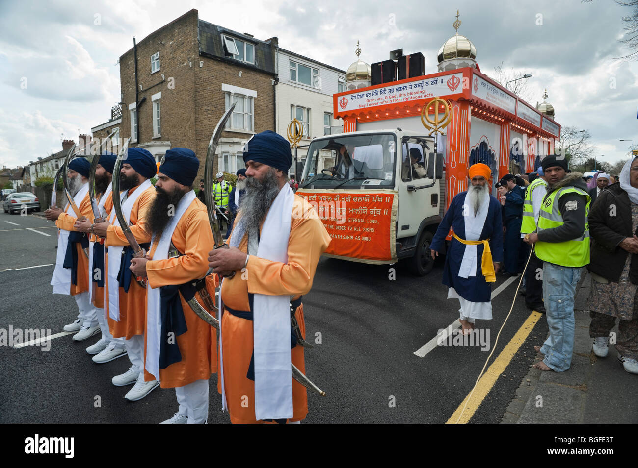 Il Panj Piyare con kirpan stand sollevata nella parte anteriore del camion che trasportano il Guru Granth Sahib in Hounslow Vaisakhi processione Foto Stock