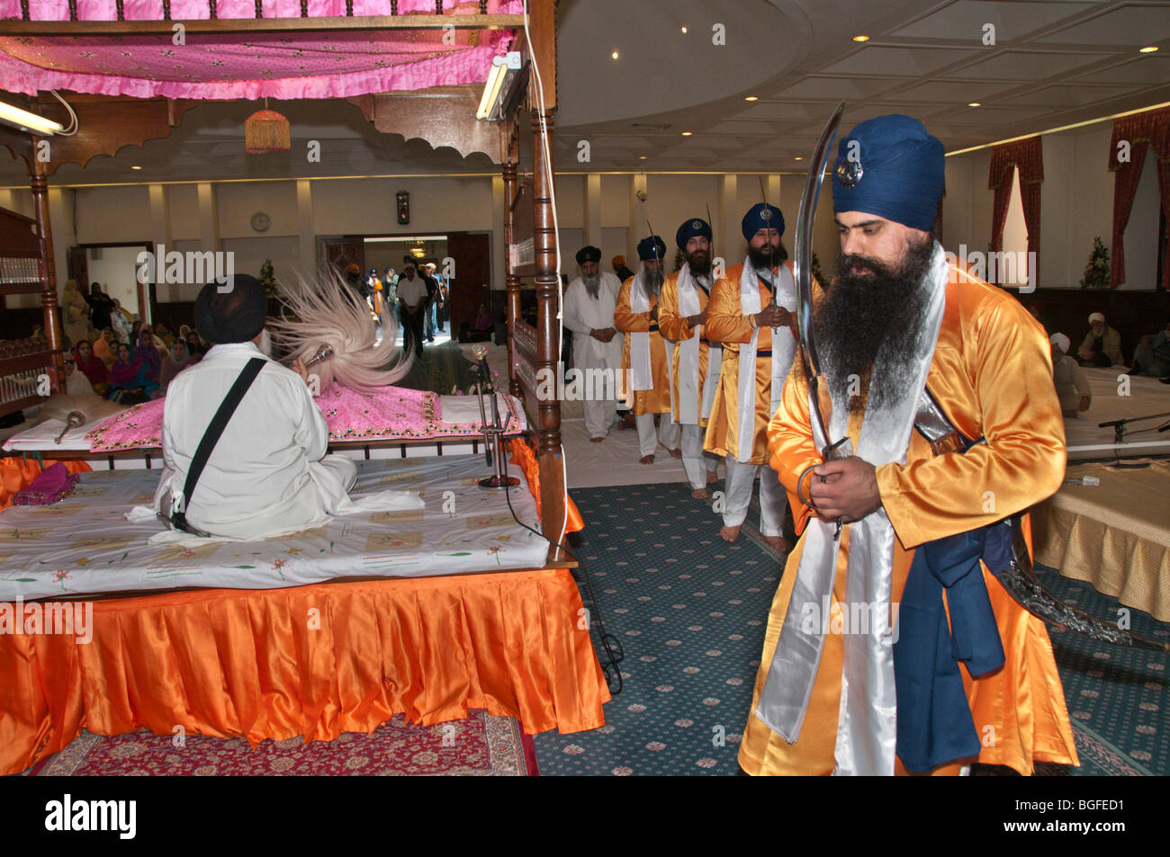 Il Panj processo Piyare dietro il Guru Granth Sahib nella sala culto durante la celebrazione Vaisakhi con kirpan sollevato Foto Stock