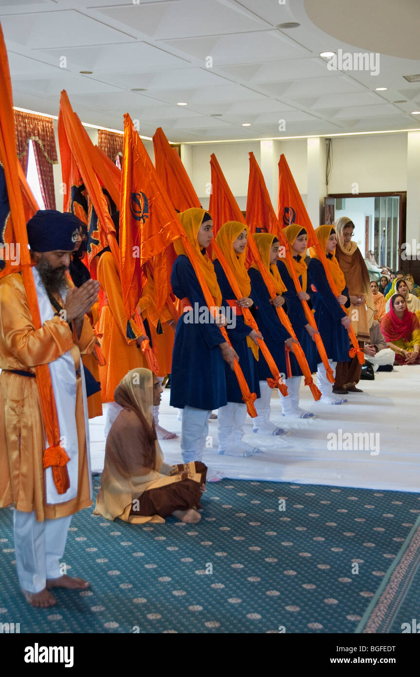 La religione sikh uomini e donne giovani con Nisan Sahib (Sikh flags) stand in preghiera nel Diwan hall durante le celebrazioni Vaisakhi Foto Stock