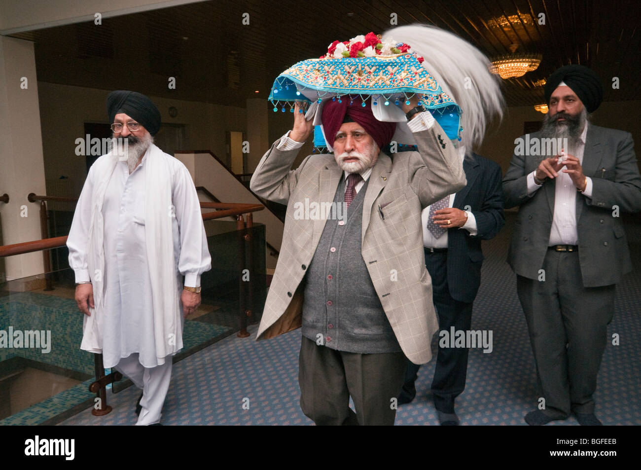 Un uomo porta il Guru Granth Sahib su un cuscino decorato nel Diwan prima che esso sia messo su la processione Vaisakhi Foto Stock