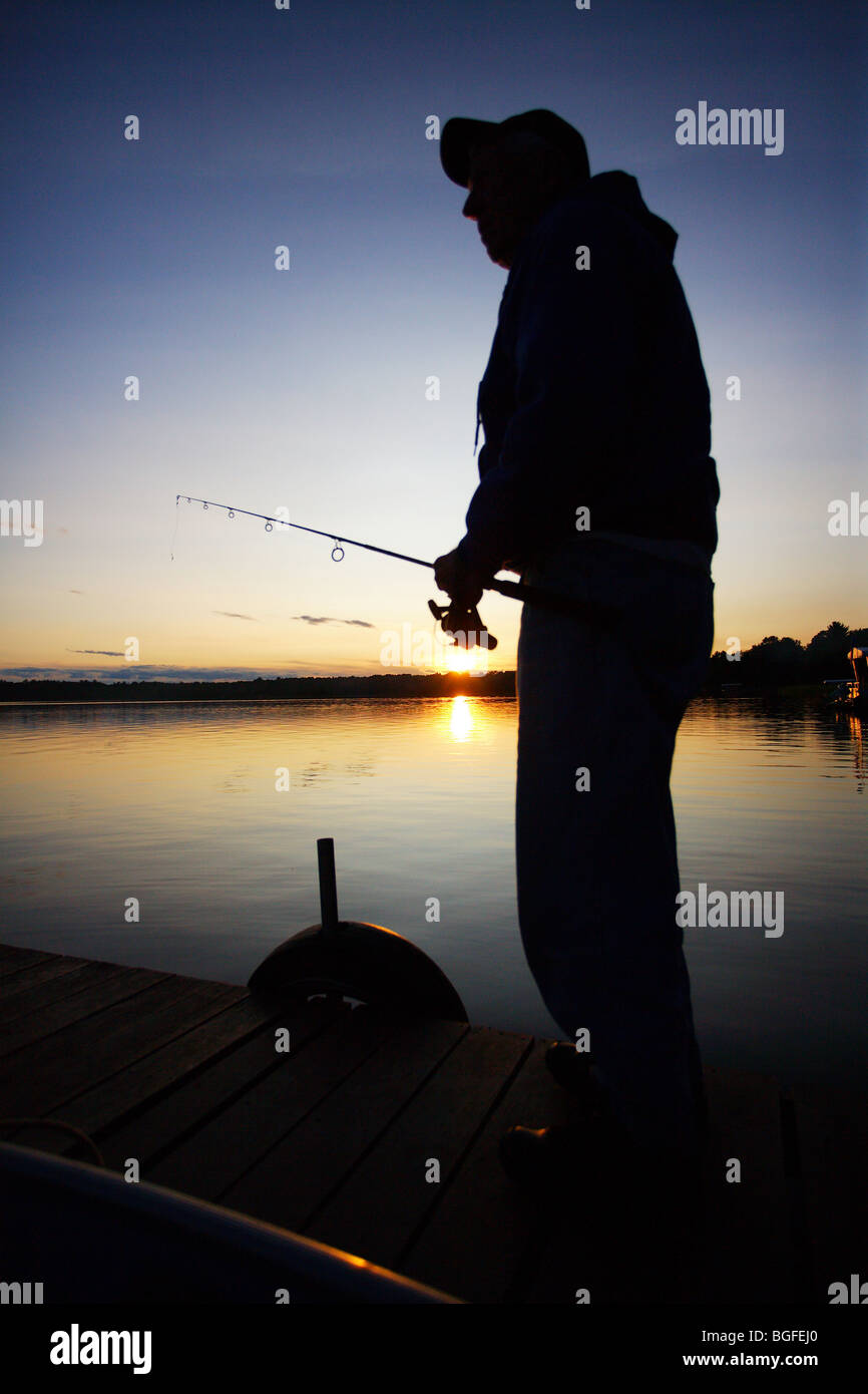 Silhouette pescatore in piedi sul molo con asta e la bobina in mano il tramonto Foto Stock