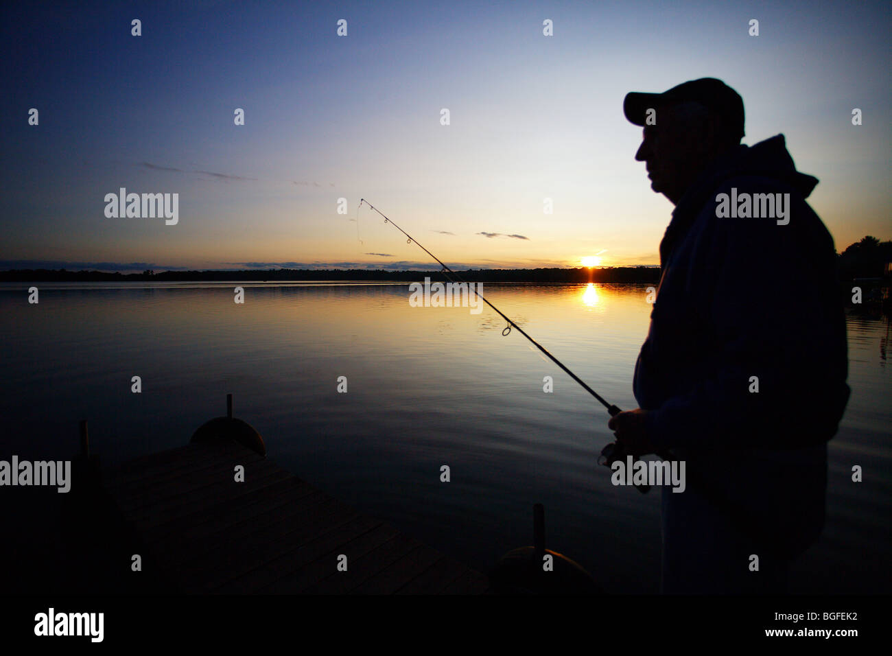 Silhouette pescatore in piedi sul molo con asta e la bobina in mano il tramonto Foto Stock