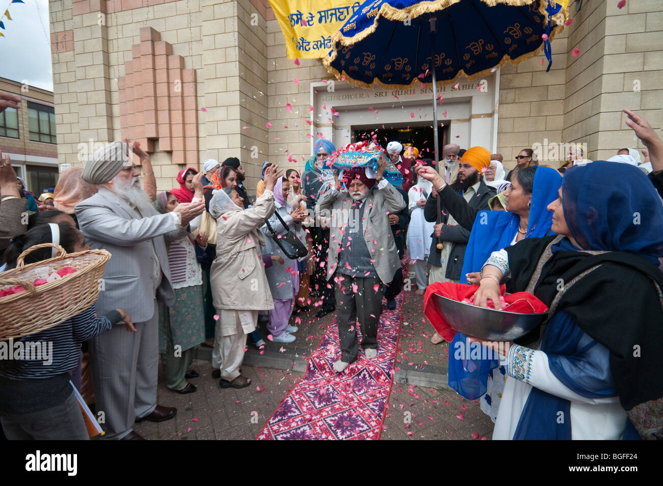 Il Guru Granth Sahib viene irrorato con petali di fiori come è portato su un uomo di testa al camion, ombreggiata da un ombrello Foto Stock