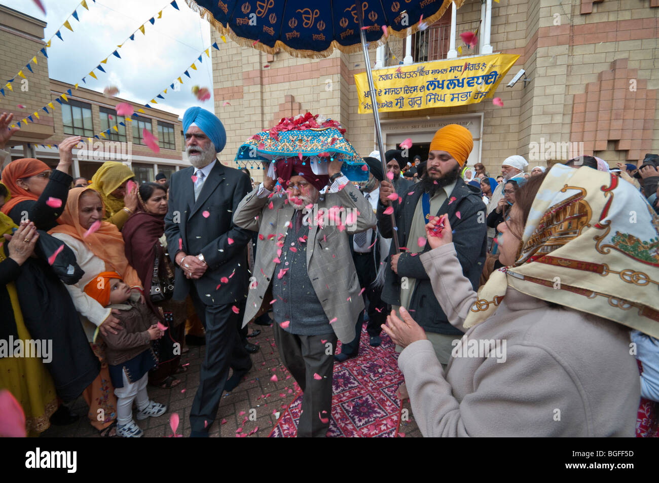 Il Guru Granth Sahib viene irrorato con petali di fiori come è portato su un uomo di testa al camion, ombreggiata da un ombrello Foto Stock