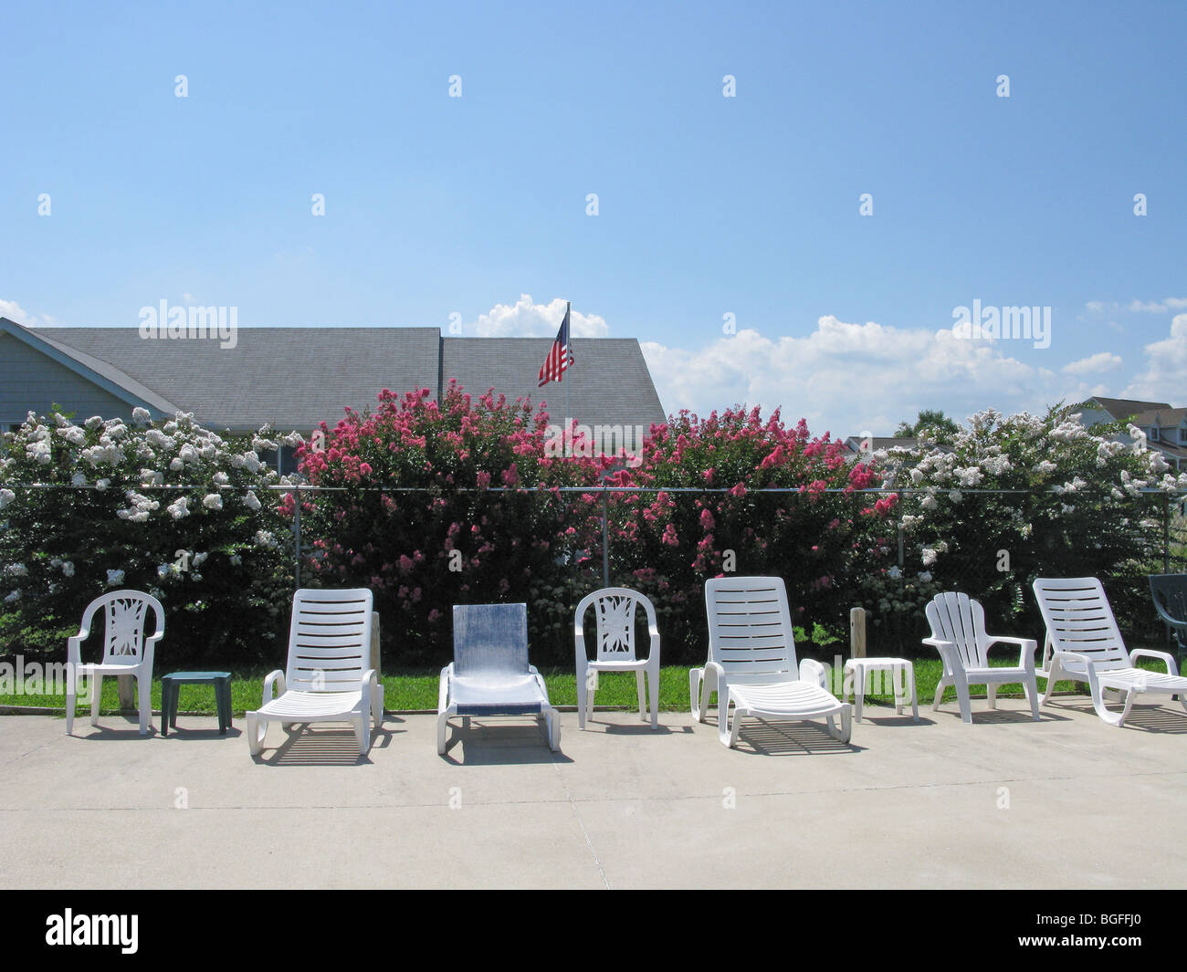 Una fila di sedie in plastica bianca, recinzione, bussole e un edificio il tetto. Foto Stock