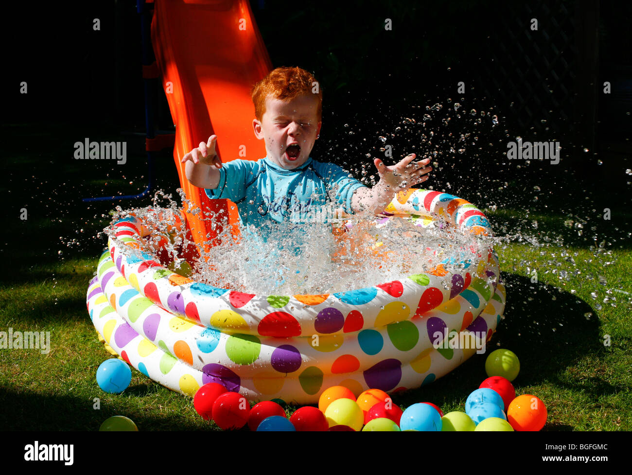 Un bambino di cinque anni, ragazzo scendendo una diapositiva in una piscinetta per bambini nel suo giardino Foto Stock