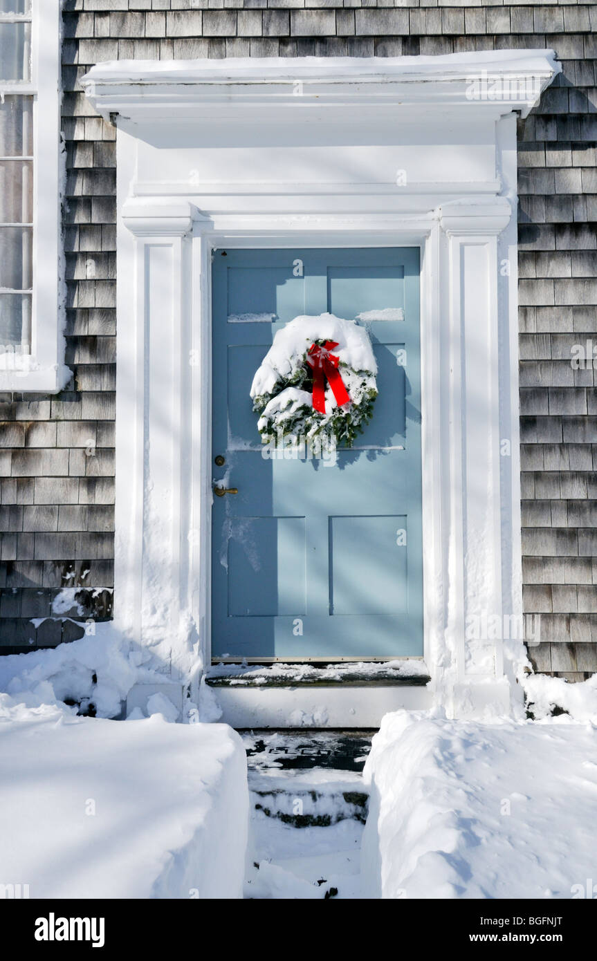Coperta di neve ghirlanda di Natale con fiocco rosso sul legno della porta anteriore con una neve shoveled cammino che conduce ad esso. Foto Stock