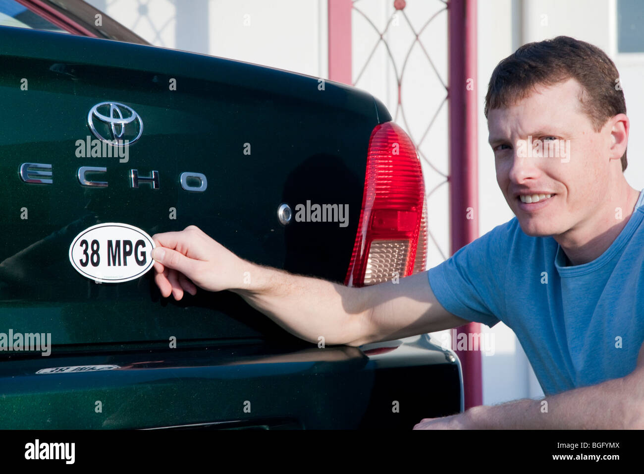 Metà uomo adulto mettendo a 38 miglia per gallone di efficienza del carburante paraurti adesivo installato su Toyota auto eco. In California, Stati Uniti d'America Foto Stock