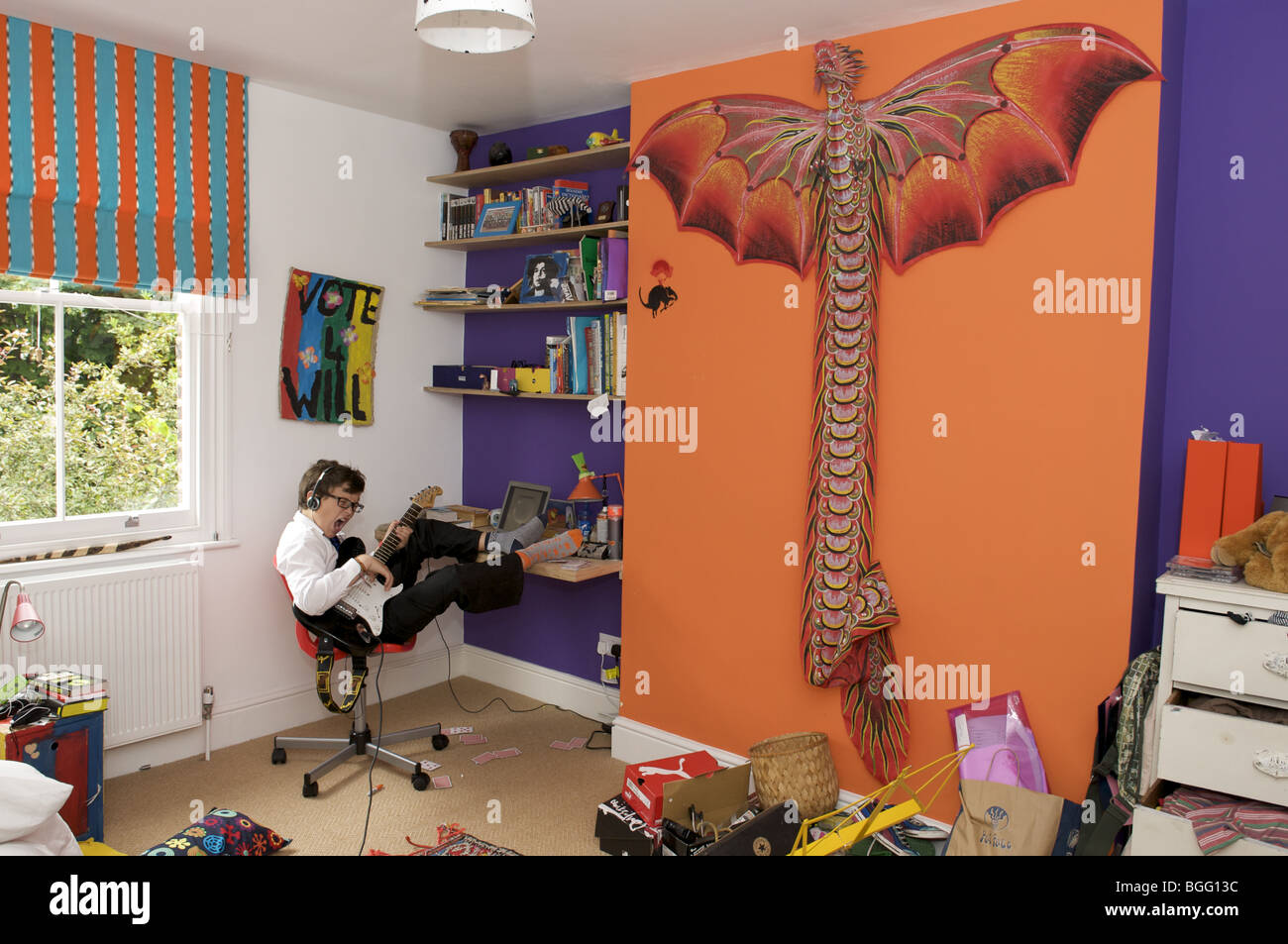 Scolaro seduto in camera da letto a suonare la chitarra Foto Stock