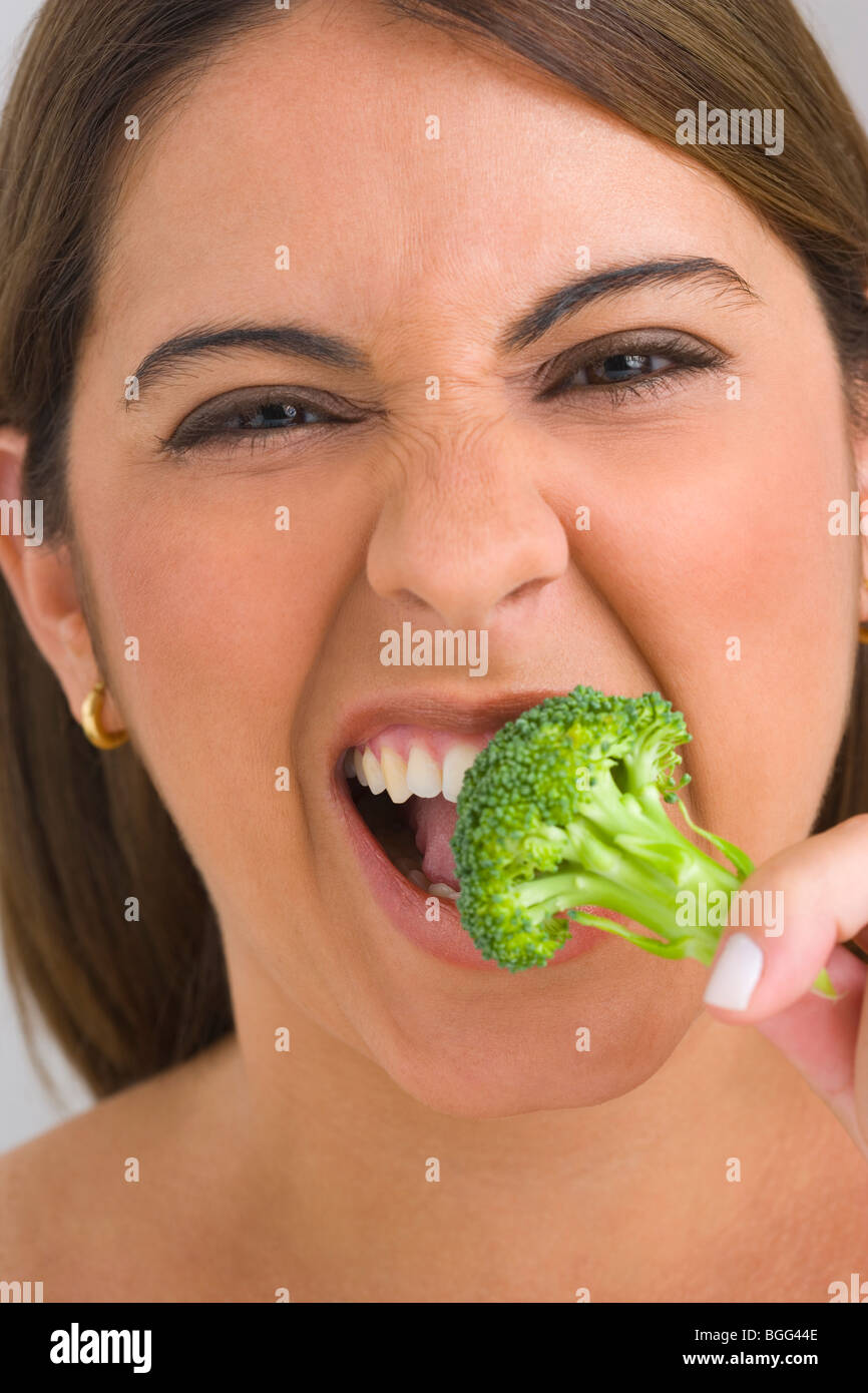 Donna di mangiare un fiorellino di broccoli con disgusto, ritratto Foto Stock